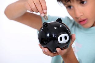 Young boy putting a £2 coin into a piggy bank.