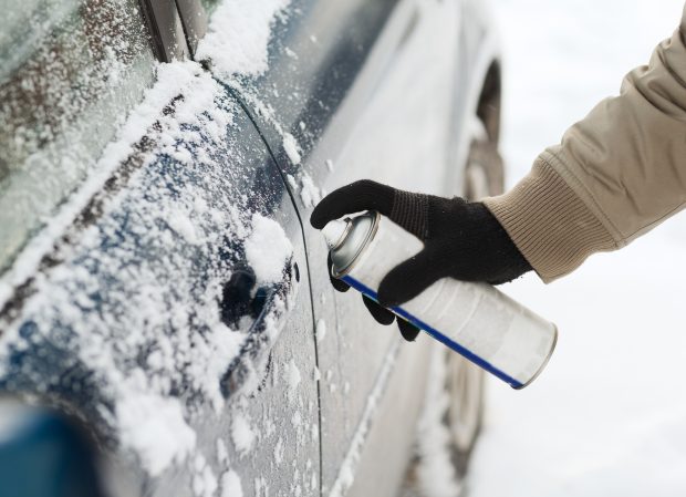 Man spraying de-icer on lock of car