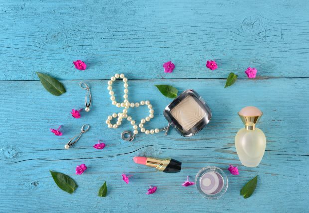 Cosmetics, perfume and jewellery lay flat on a blue background.