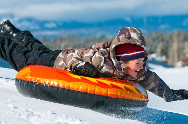 A smiling boy having fun sleding on a tube in the snow.