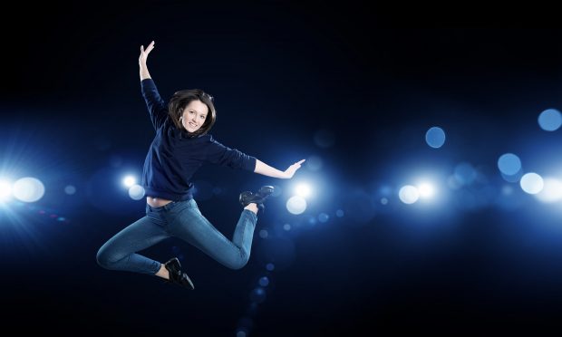 Young woman dancer jumping in spotlights on dark background