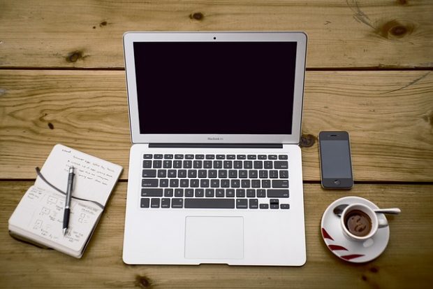 Laptop, mobile phone, notepad and cup of coffee on wooden desk