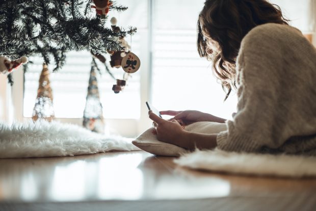 Woman lying next to christmas tree using smart phone