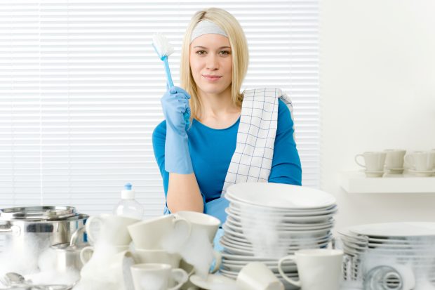 Woman stood in front of a pile of dishes, holding a scourer