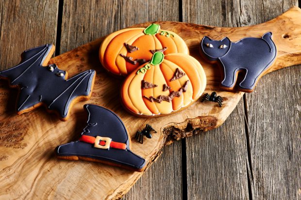 Halloween cookies including a bat, pumpkin, cat and witches hat, displayed on a wooden board