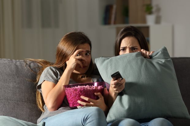 Two scared looking girls sitting on sofa watching horror film