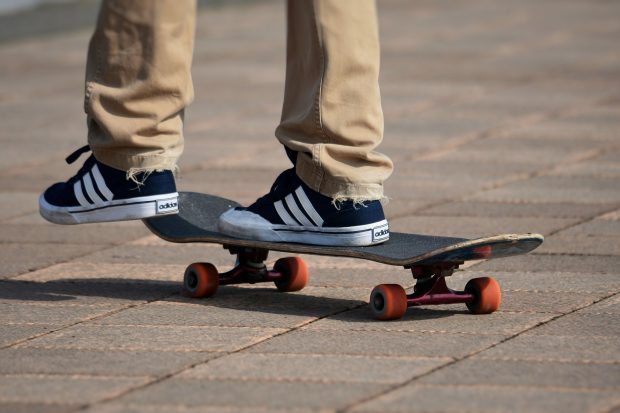 Person on skateboard wearing navy Adidas trainers with white stripes