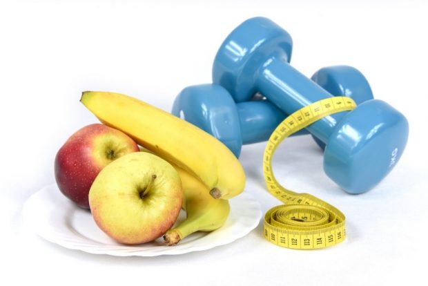 Apples and banana on plate with a tape measure resting on two dumbells