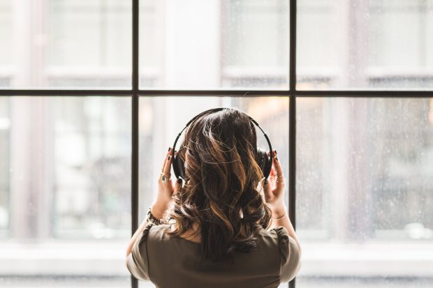 Woman looking out a window wearing headphones.