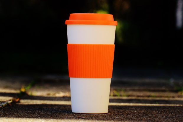 A re-useable orange and white coffee flask on a pavement.