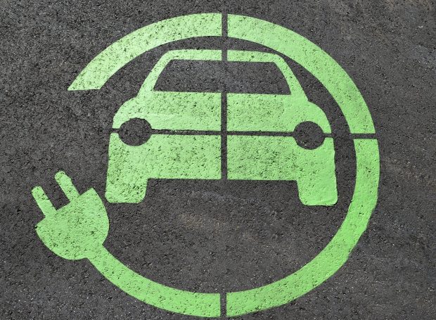 Green electric charge road sign on tarmac showing a car with an electric charge cable circling it.