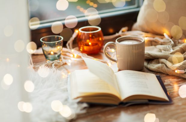 A book, cup of hot chocolate and candles with garland on window sill