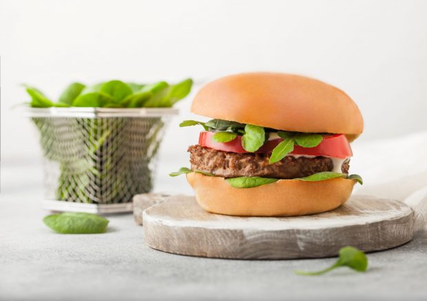 Vegetarian meat free burger on round chopping board with vegetables in mini chip basket