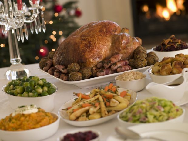 Christmas dinner with turkey, vegetables and all the trimings on a white tablecloth with roaring fire and christmas tree in the background