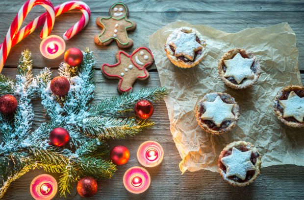 Mince pies, gingerbread men and candy canes on a table, with decorated Christmas tree branch