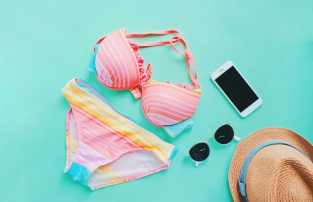 Flat lay of summer items with colorful bikini, sunglasses , hat and smartphone on green background, copy space