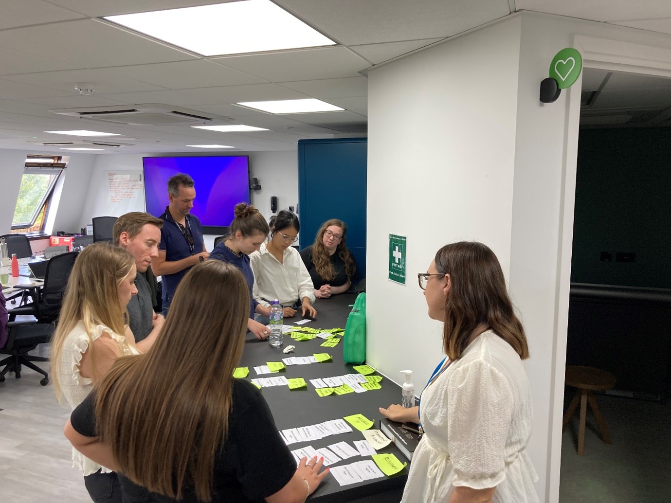 Eight people standing around a desk looking at paper 