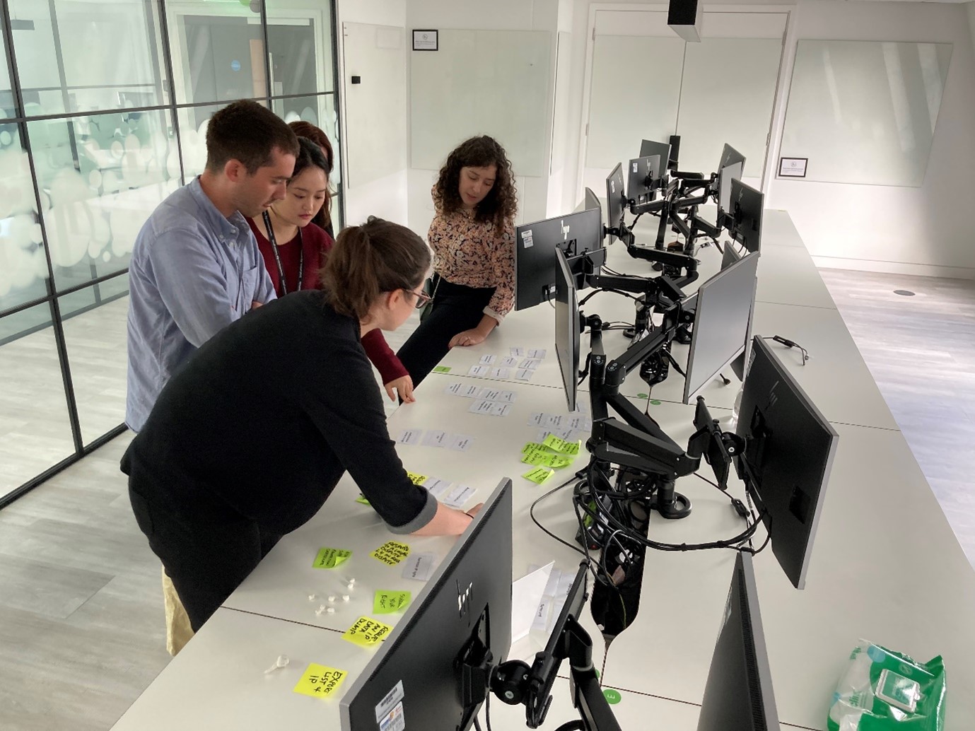 People standing at desk with computer monitors looking at paper 