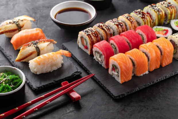 Sushi rolls set, nigiri sushi and soy sauce on a black textured background and chopsticks on the side. Traditional Japanese food, angle view.