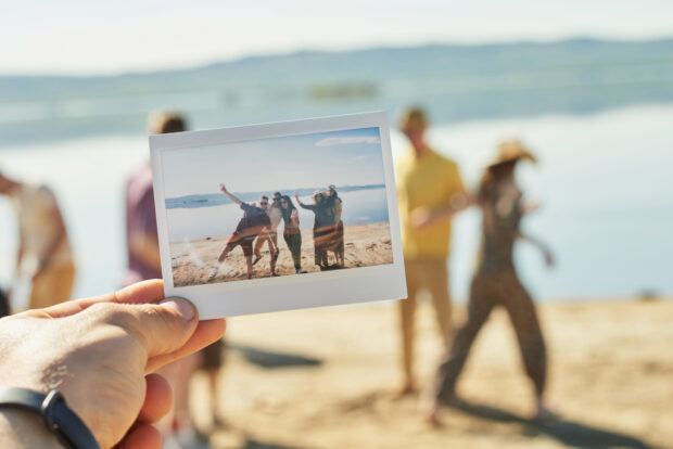 Close-up view of hand holding polaroid photo print with people on a beach
