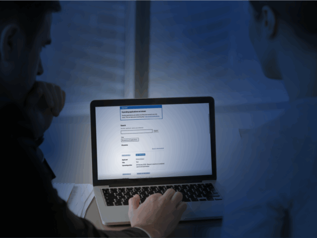 An image of 2 people looking at a laptop screen, showing a gov.uk page.