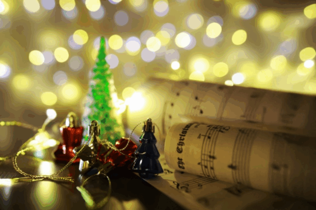 A closeup image of Christmas decorations with sheet music and blurred lights in the background