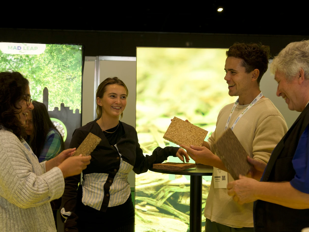 Co-founders Caelo Dineen Vanstone and Hugo Knox smiling and holding their business material as they chat to two other people.