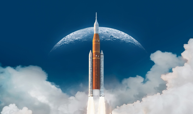A space rocket on a NASA mission blasts off through blue sky and clouds silhouetted against the distant orb of a silvery white moon.